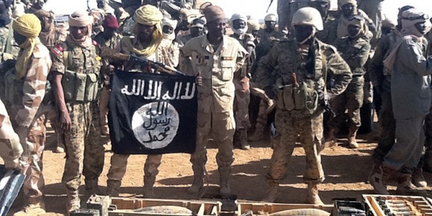 Soldats tchadiens posant avec un drapeau d'Aqmi et des munitions qu'ils ont récupérées à Tessalit, dimanche 3 mars. (Ali Kaya - AFP)