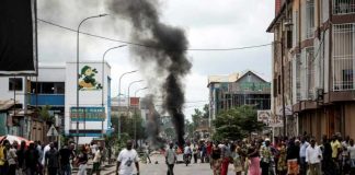 Des Kinois regardent des manifestants brûler des pneus au cours d'une marche anti-Kabila à Kinshasa, le 21 janvier 2018. / © AFP / JOHN WESSELS