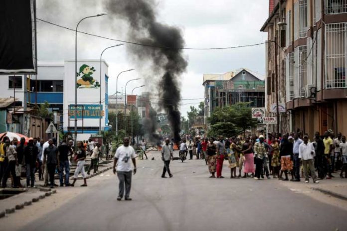 Des Kinois regardent des manifestants brûler des pneus au cours d'une marche anti-Kabila à Kinshasa, le 21 janvier 2018. / © AFP / JOHN WESSELS